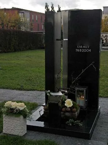 Dunkle Grabstele mit senkrechtem Metallkreuz und bepflanztem Sockel