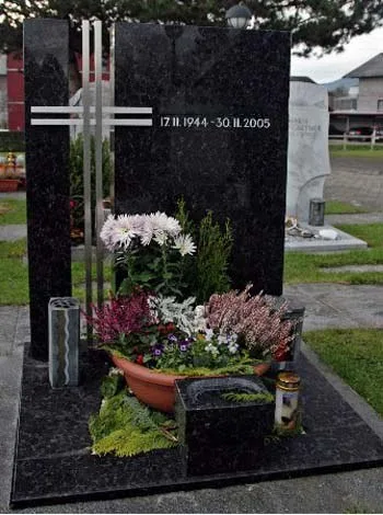Grabmal aus blau geflammtem Granit mit hellem Kreuz und Blumenschale