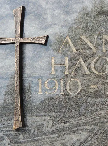Gravierte Schrift neben einem Bronzekreuz auf hellem Granit