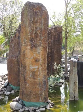 Drei Brunnenstelen aus Naturstein in einem Wasserbecken mit Kieselrand