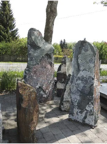 Drei rohe Findlinge nebeneinander auf gepflastertem Grund